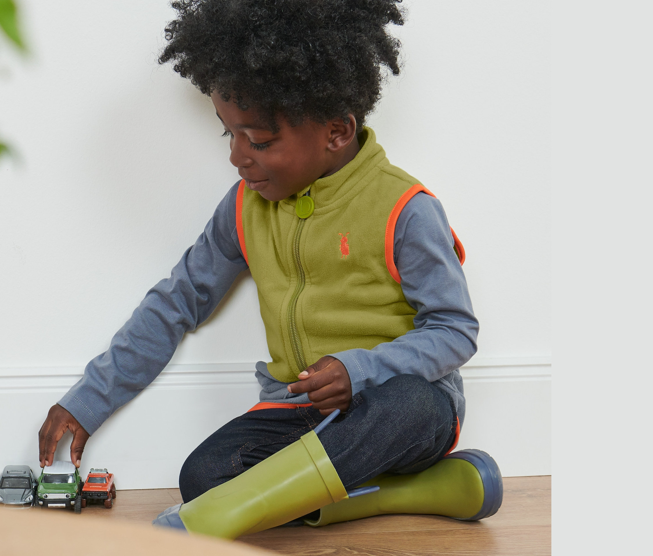 Chlapec sa hrá s autíčkami na podlahe a má na sebe detskú flísovú vestu, kombinácia kontrastných farieb.