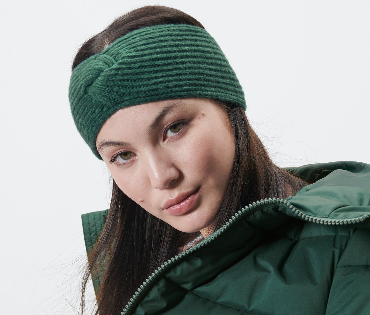 Žena má na sebe pletenú čelenku tmavozelenej farby a zelenú bundu.