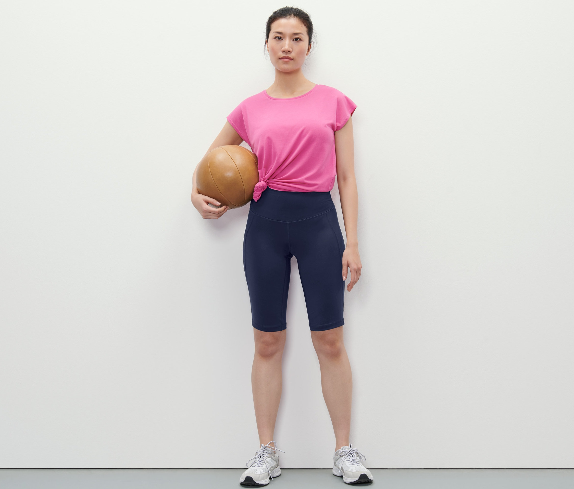 Žena drží basketbalovú loptu a má na sebe tmavomodré športové cyklistické šortky.