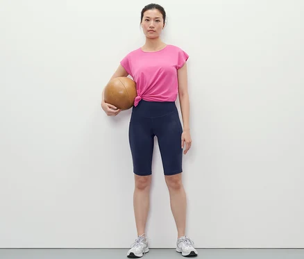 Žena drží basketbalovú loptu a má na sebe tmavomodré športové cyklistické šortky.