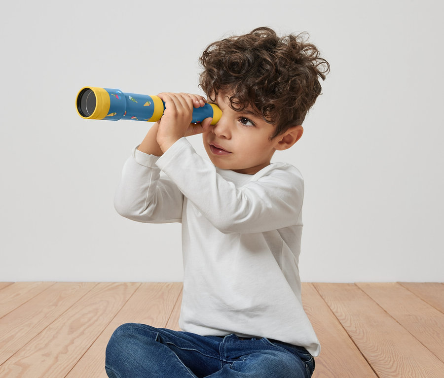 Chlapec sedí na podlahe a pozerá cez hračkársky teleskop.