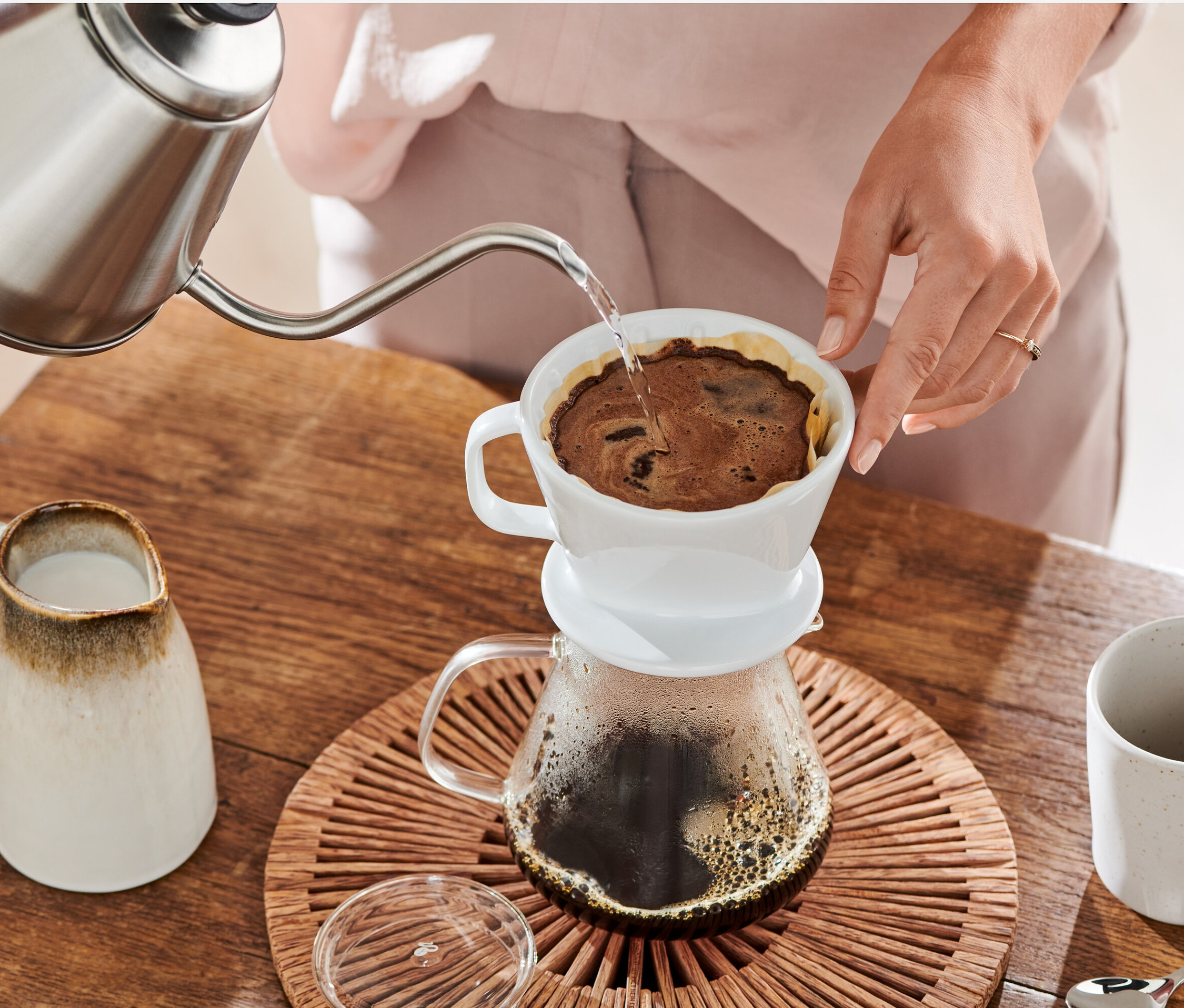 Žena naleje vodu z kanvice do bieleho ručného filtra na kávu, veľ. 2 s papierovým filtrom veľ. 2, biely, 18x 80 ks.