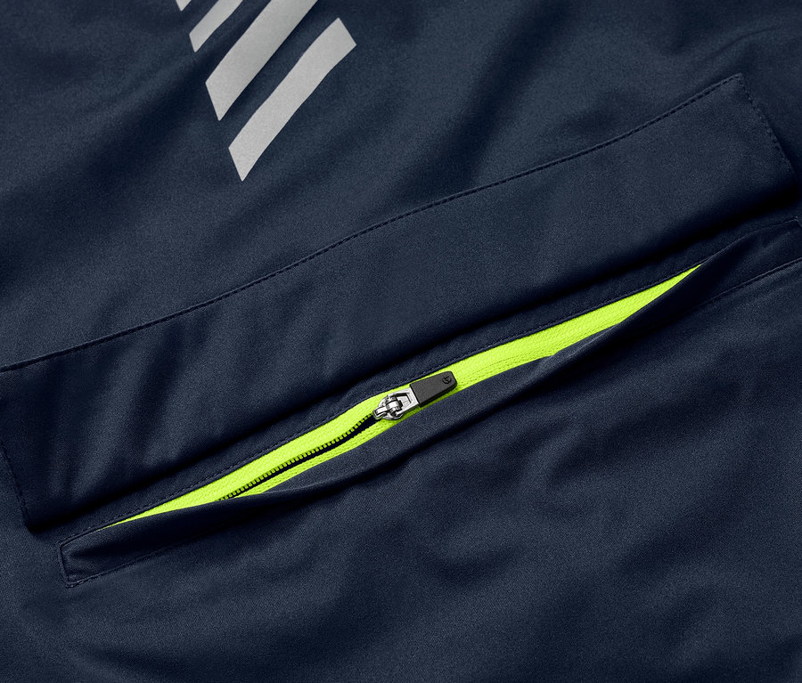 Detail modrej cyklistickej vetrovky Rad-Regenjacke s neónovo zeleným zipsom na vrecku a reflexnými prvkami.