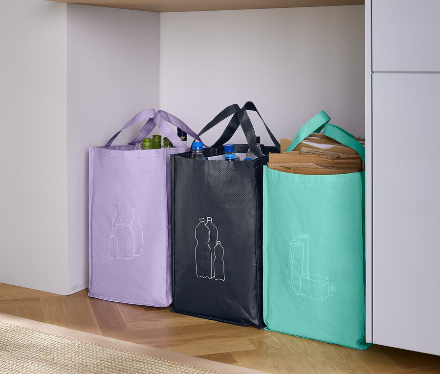 Tri nákupné tašky stoja vedľa seba: fialová taška s nákresom ovocia, čierna taška s nákresom fliaš a tyrkysová taška s nákresom pohára.