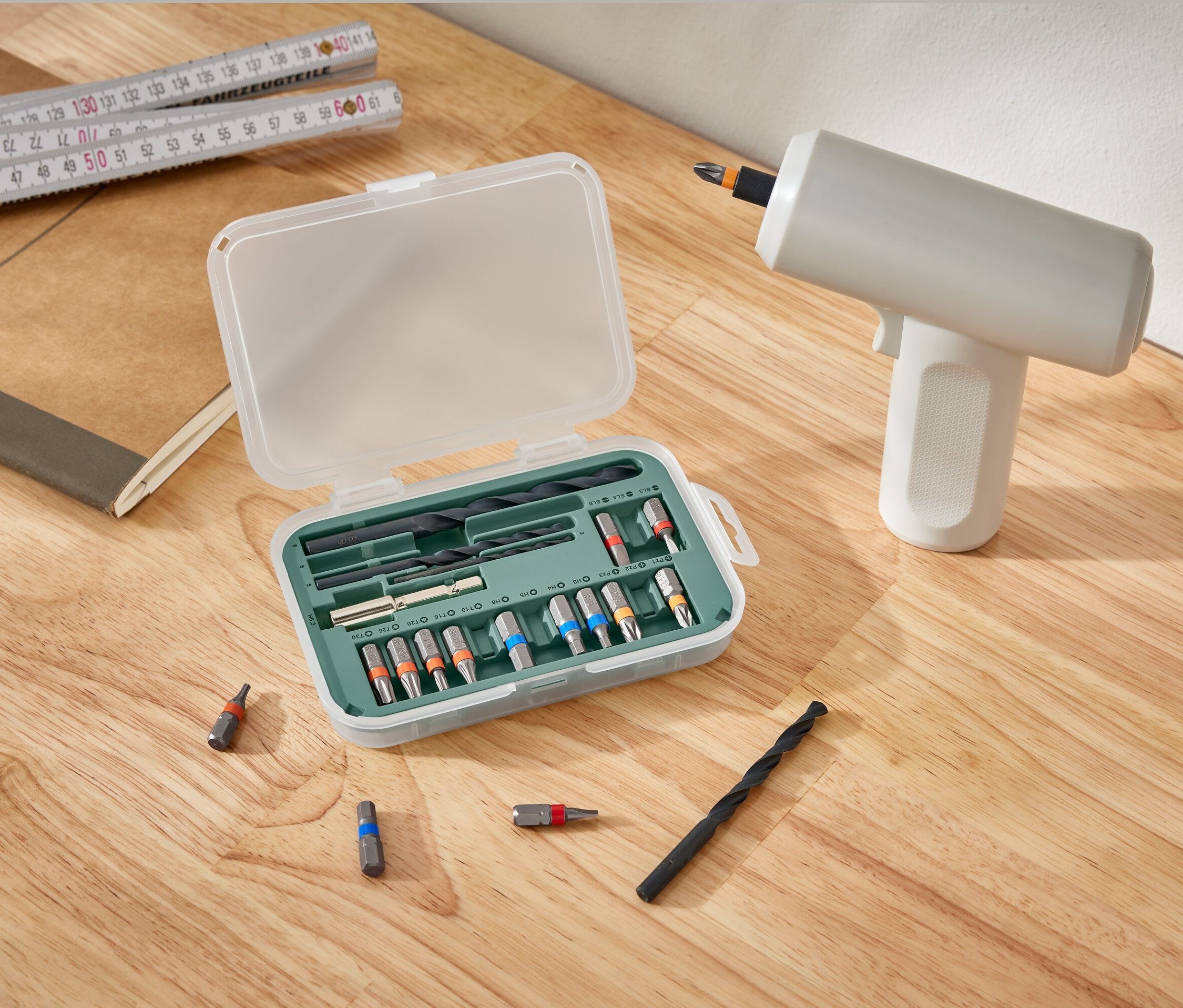 Súprava pre skrutkovače a vŕtačky leží otvorená vedľa vŕtačky na drevenom stole.