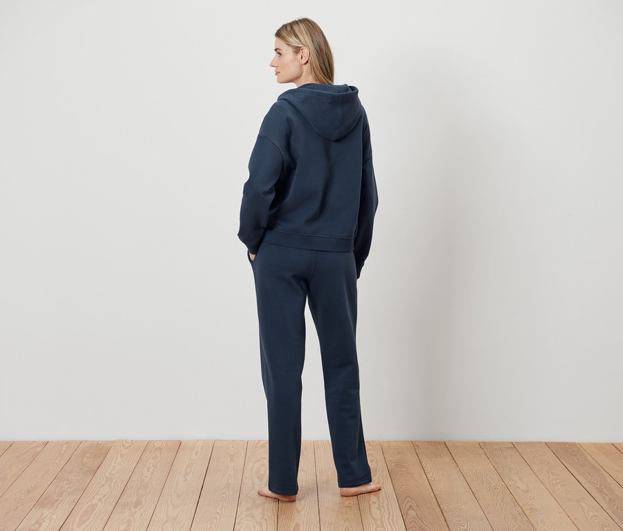 Žena stojí chrbtom, má na sebe tmavomodrú mikinu s kapucňou a tepláky.