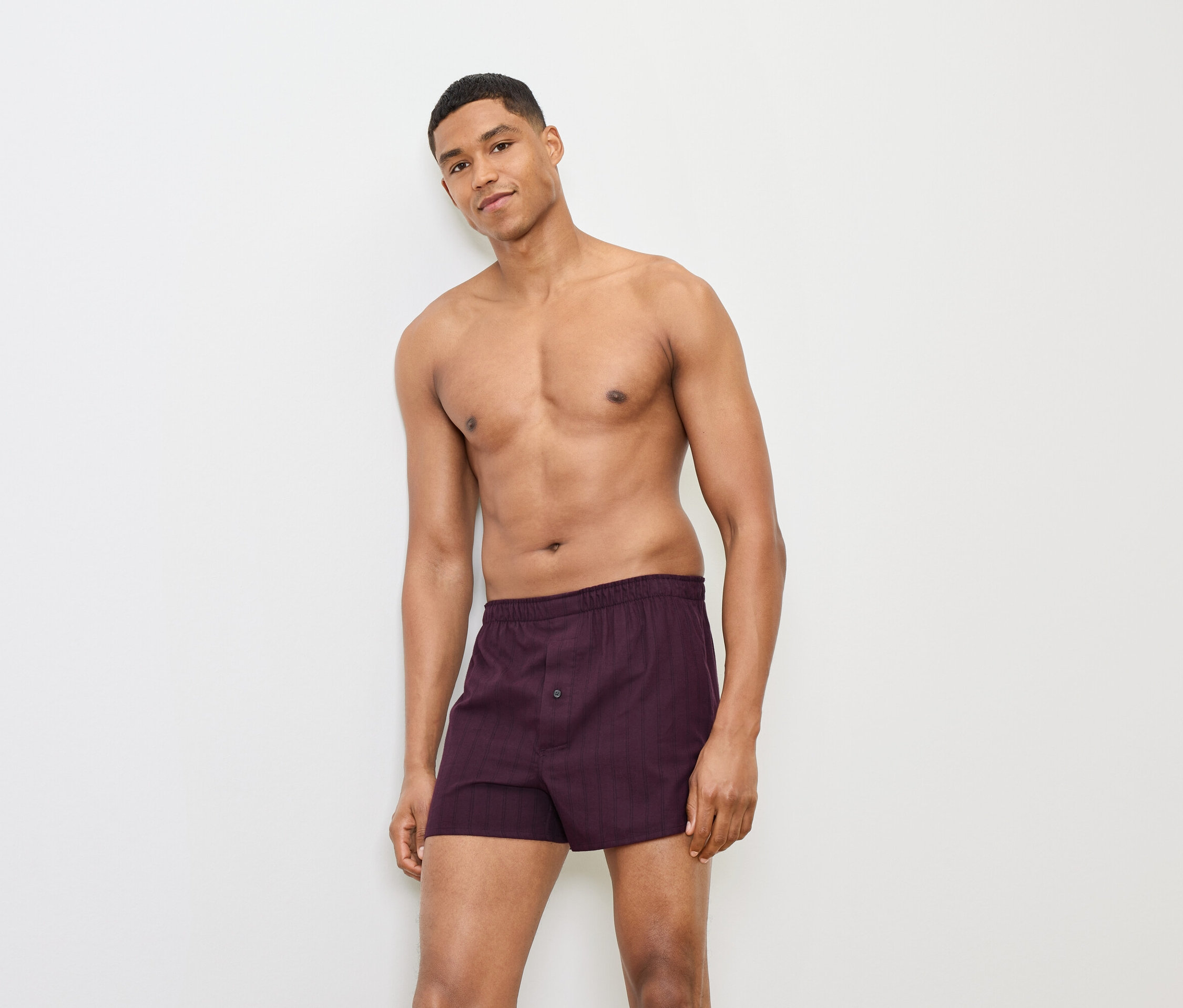 Muž pózuje v bordových boxerkách pred bielym pozadím.