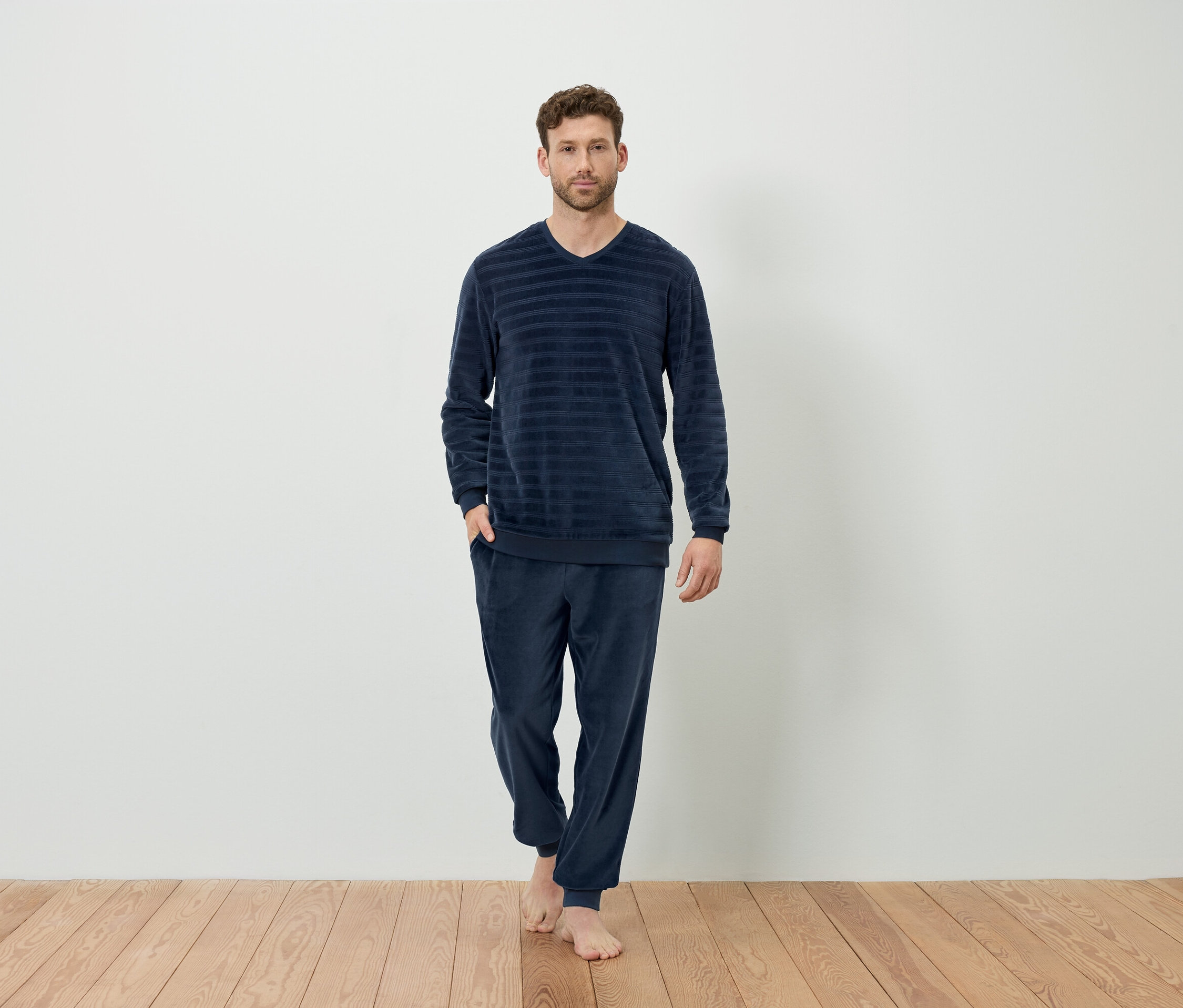 Muž stojí bosý a má na sebe tmavomodré, pásikavé pyžamo.