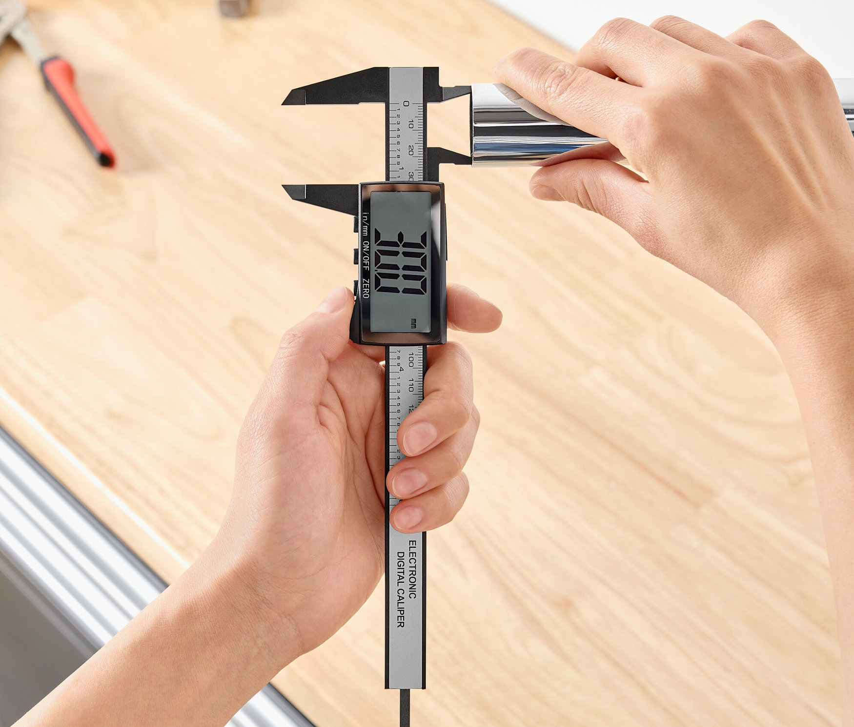 Osoba meria priemer kovovej rúrky pomocou digitálneho posuvného meradla.