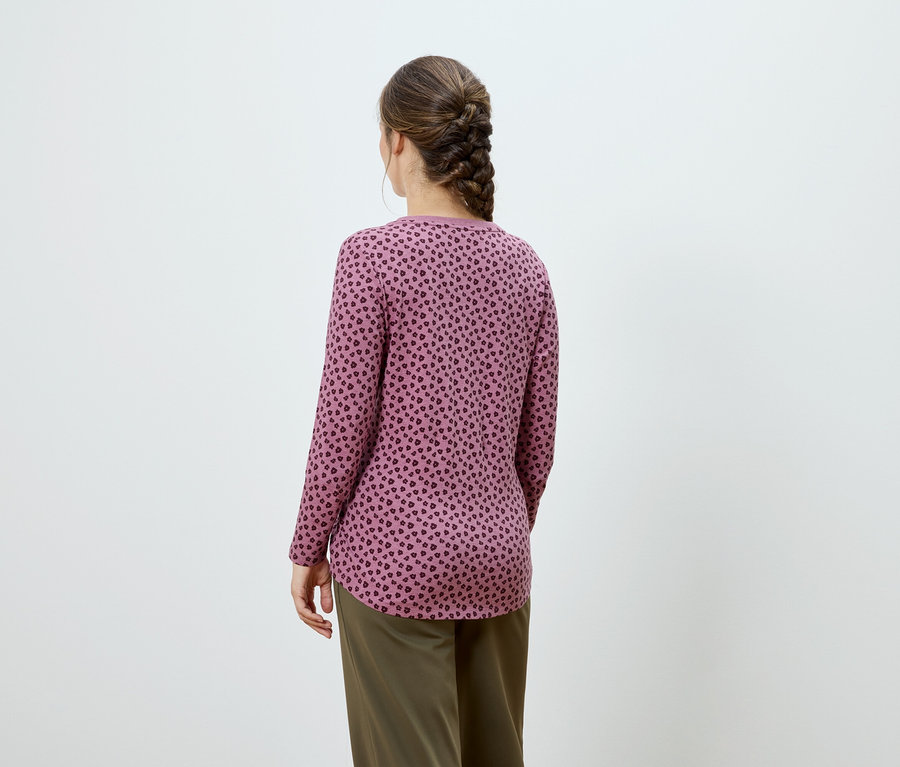 Pohľad zozadu na ženu s hnedým vrkočom, oblečenú v ružovom tope s dlhými rukávmi a tmavou potlačou a khaki nohaviciach.