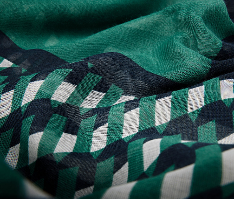 Detailný záber na látku so vzorom zelených a bielych geometrických tvarov na tmavomodrom pozadí.