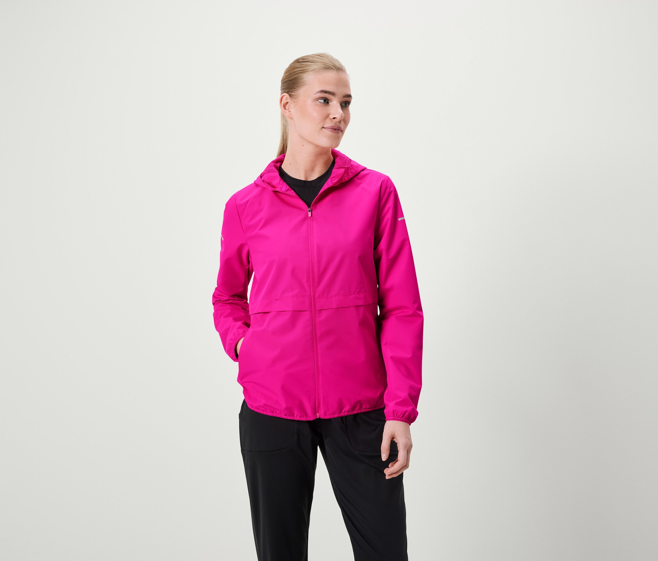 Žena má na sebe ružovú bundu s kapucňou a čierne nohavice.
