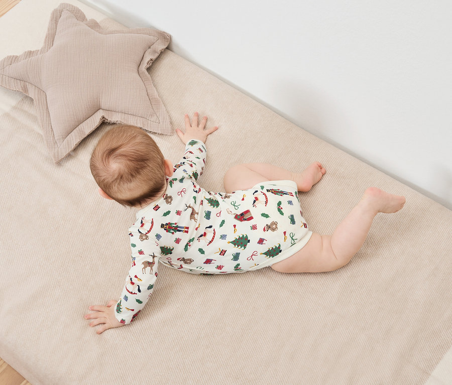 Dieťa leží na bruchu na deke s vianočnou potlačou vedľa béžového hviezdicového vankúša.