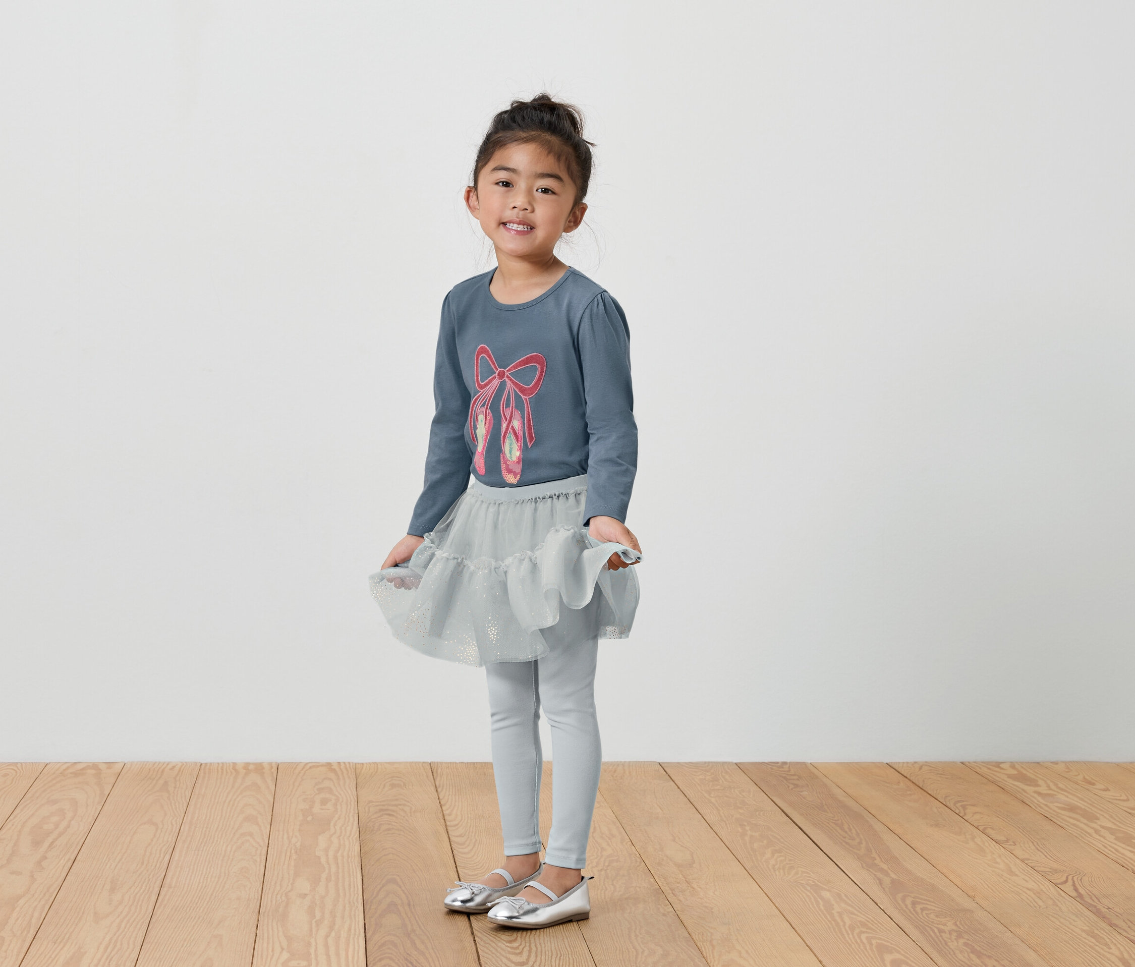 Dievča v sivom baletnom oblečení s tričkom, sukňou a legínami.