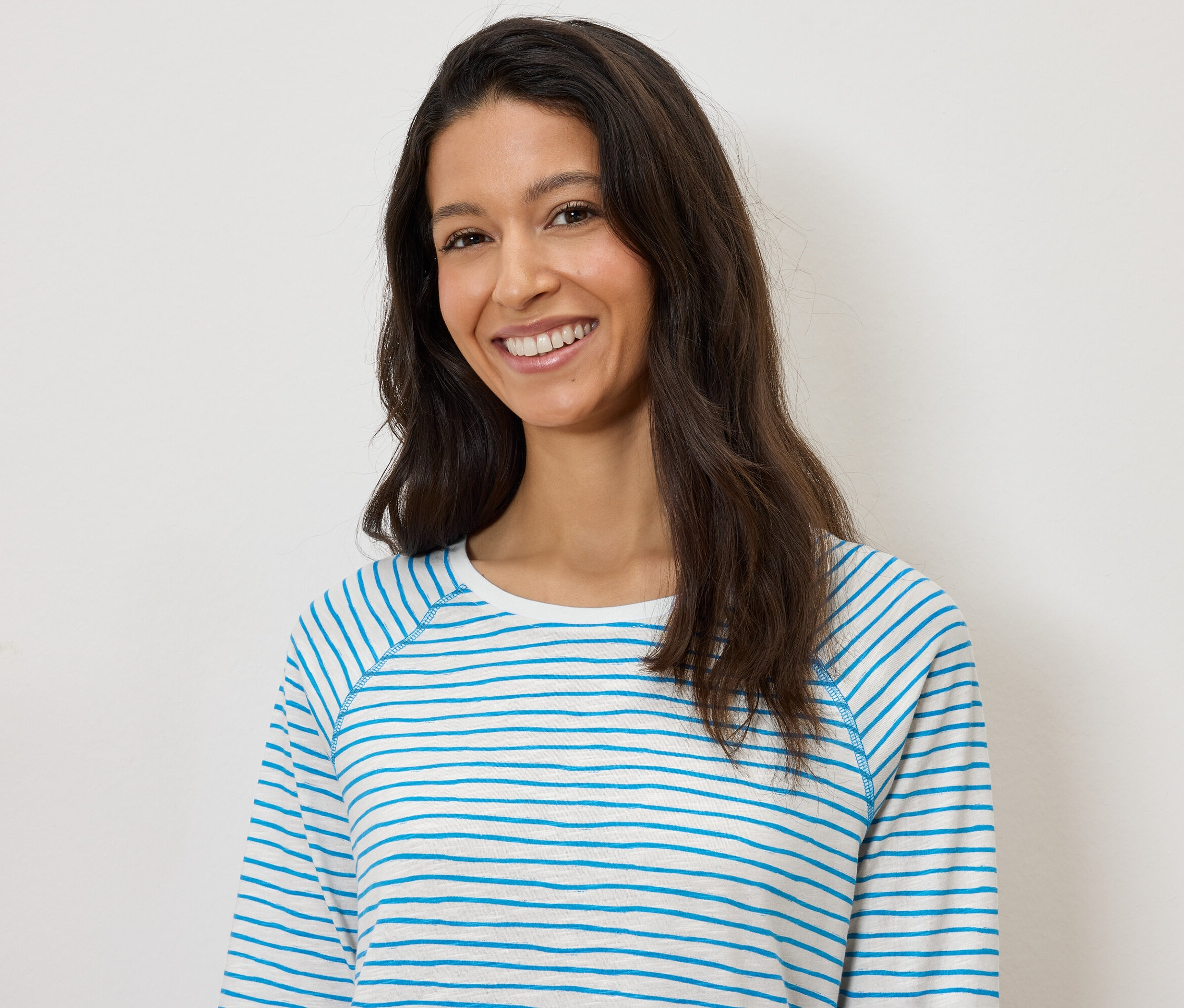 Žena sa usmieva a má na sebe modro-biele pruhované tričko s dlhým rukávom na bielom pozadí.