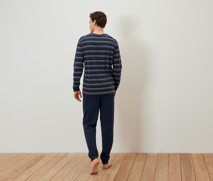 Muž v pruhovanom pyžame ide bosý po drevenej podlahe.