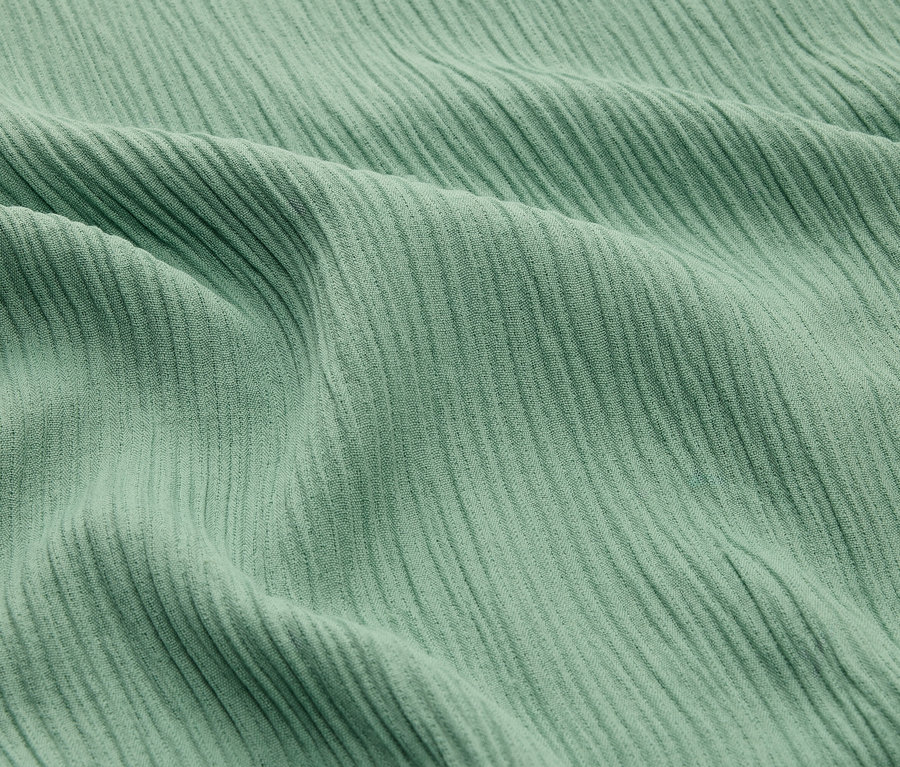 Detailný záber mätovo zelenej rebrovanej látky so záhybmi.