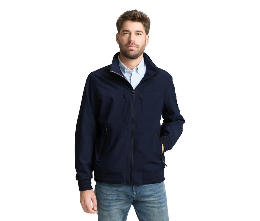 Muž v bunde Tom Tailor bomber, Sky Captain modrá a džínsy, s jednou rukou vo vrecku.