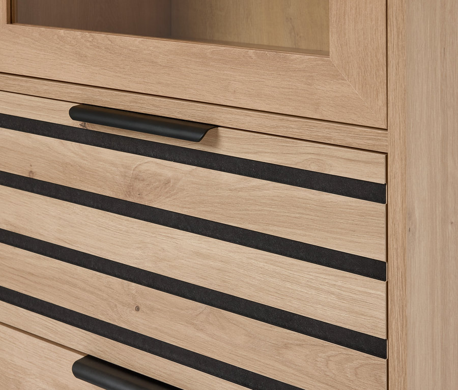 Detailný záber svetlohnedej drevenej skrinky so zásuvkami s čiernymi vodorovnými akcentmi a čiernymi vodorovnými úchytkami.