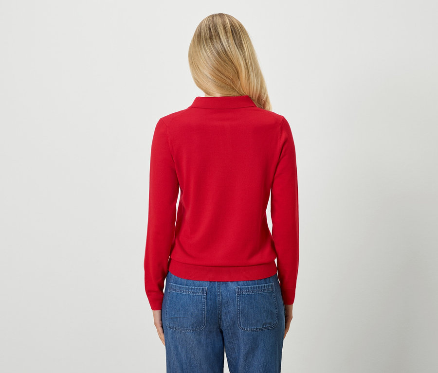 Pohľad zozadu na ženu s blond vlasmi v červenom svetri a modrých džínsoch.