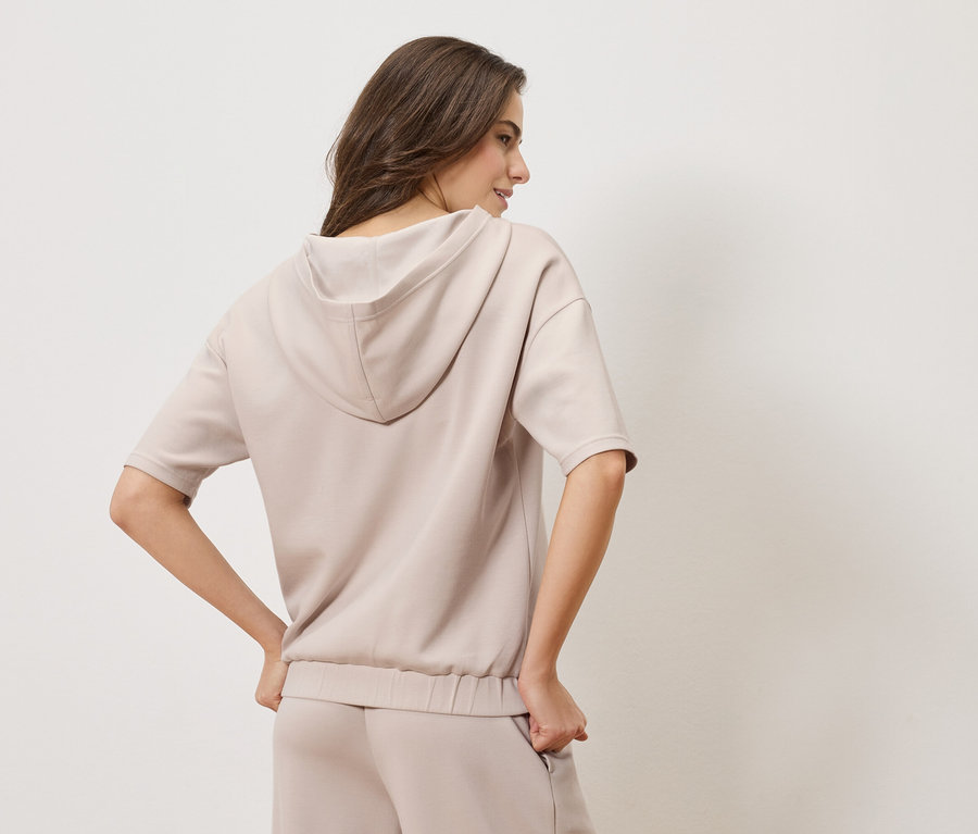 Žena zozadu v béžovej mikine s kapucňou a zladených nohaviciach.
