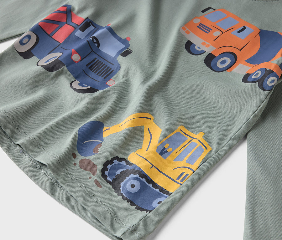 Detailný záber svetlozelenej košele s dlhým rukávom s potlačenými stavebnými autami.