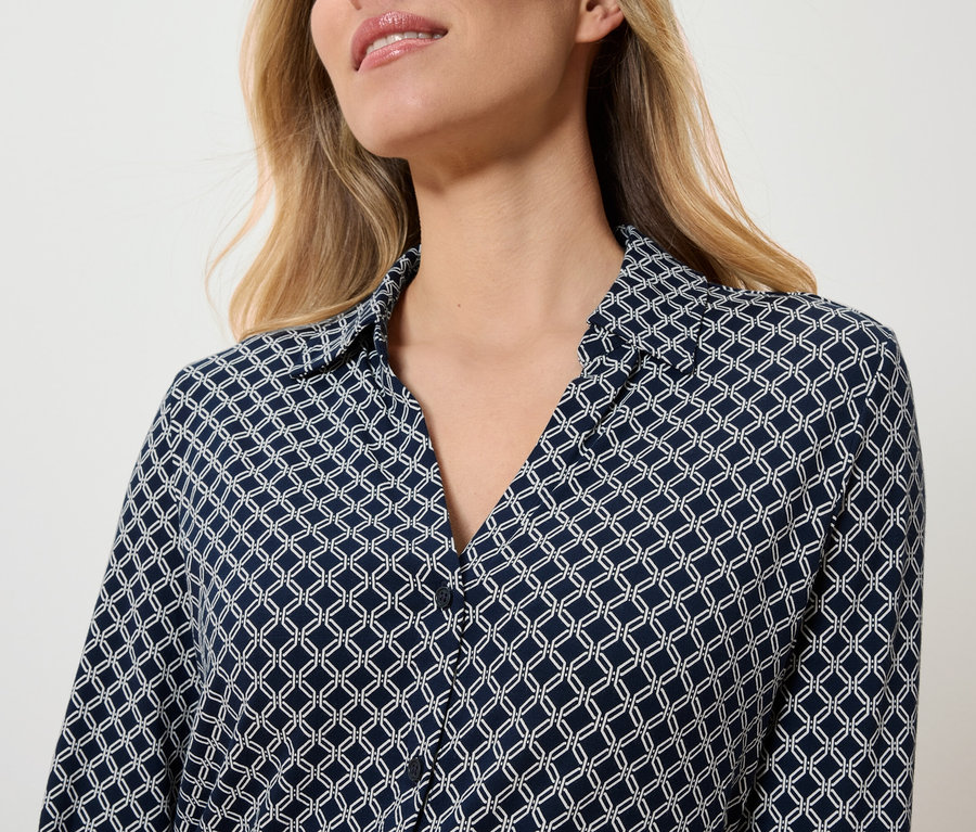 Horná časť tela ženy v tmavomodrej blúzke s bielym geometrickým vzorom.