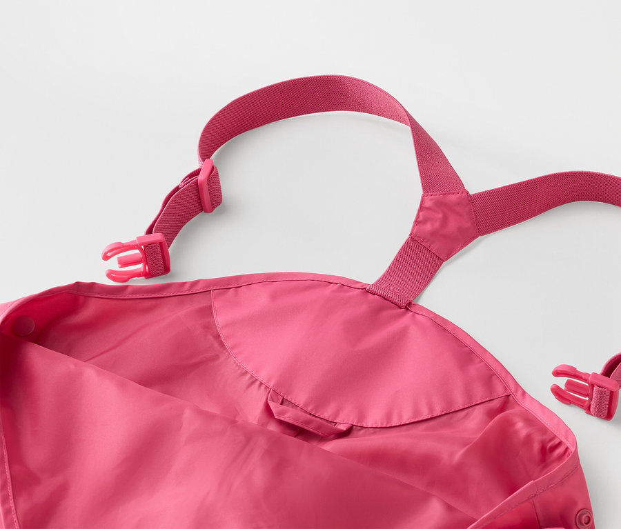 Detail ružových detských nepremokavých nohavíc s nastaviteľnými ramienkami a prackami na bielom pozadí.