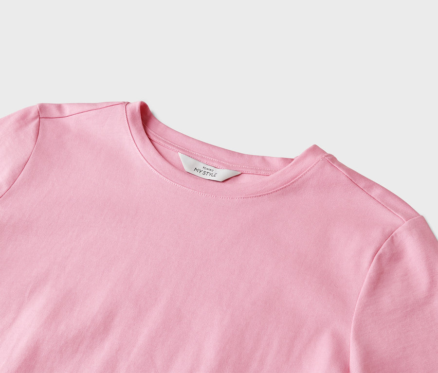 Detailný záber na svetloružové tričko s okrúhlym výstrihom a bielym štítkom s nápisom „Tchibo My Style“.