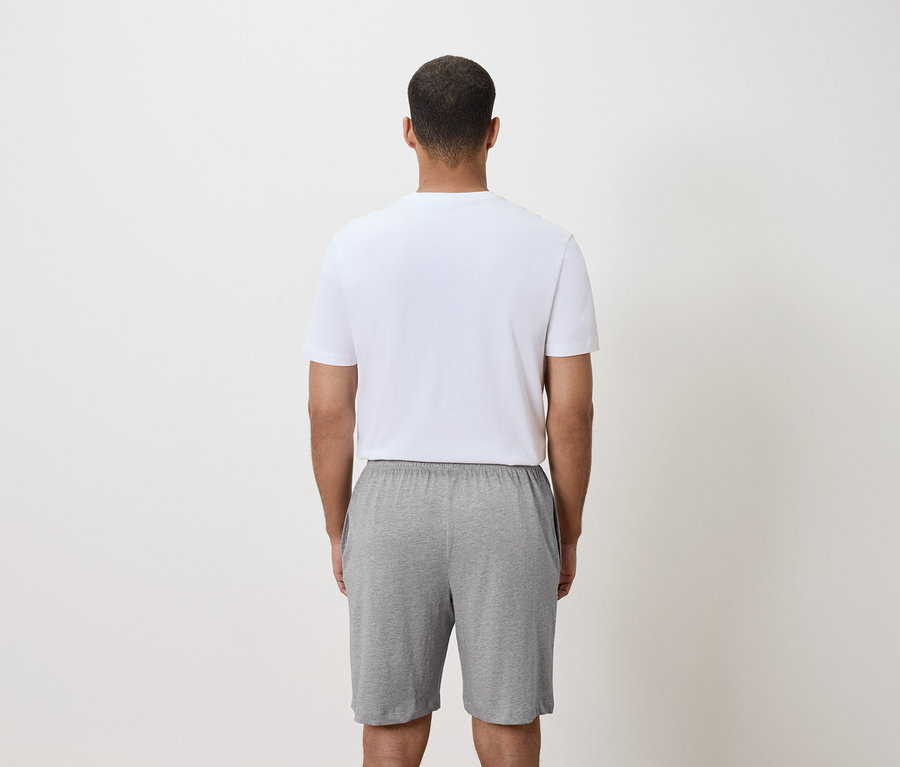 Pohľad zozadu na muža v bielom tričku a sivých šortkách.
