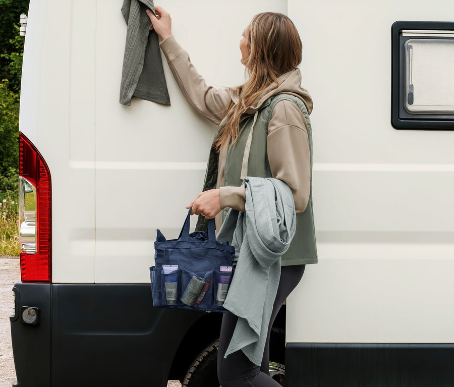 Žena vešia sivozelený mušelínový uterák na karavan, drží tmavomodrú toaletnú tašku a ďalší svetlosivozelený mušelínový uterák.