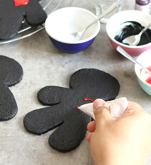 Cookies in Form von Vodoopuppen werden mit Lebensmittelfarbe dekoriert