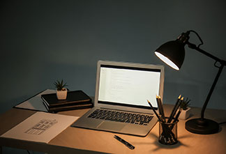 Správne miesto na svetlo: na drevenom písacom stole stojí vedľa laptopu čierna kancelárska lampa.