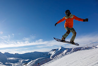 Športové bundy na zimu: snowboardista pri skoku v zasnežených horách